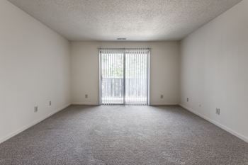 An empty living room with a sliding glass door to a balcony